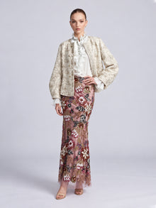 A model wears a light-colored Floral Appliqué Embroidered Jacket by Social Queen over a white ruffled blouse and a floor-length pink skirt with floral embroidery and beadwork.