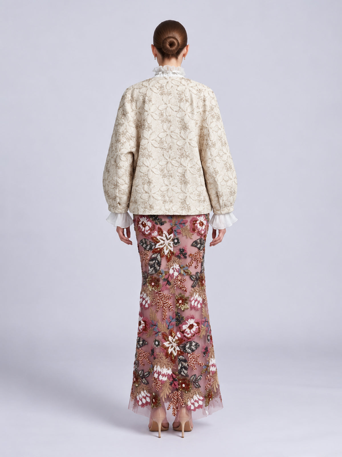 Back view of a person wearing a cream-colored Floral Appliqué Embroidered Jacket by Social Queen over a floor-length sheer skirt with colorful floral embroidery and beadwork.