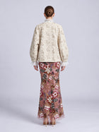 Back view of a person wearing a cream-colored Floral Appliqué Embroidered Jacket by Social Queen over a floor-length sheer skirt with colorful floral embroidery and beadwork.