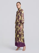 A woman stands in profile against a plain background, wearing the Social Queen Art Floral Jacquard Maxi Dress—a long-sleeved, floor-length gown featuring a yellow and purple floral pattern.