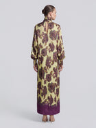 A woman with her hair in a bun models the Social Queen Art Floral Jacquard Maxi Dress, a long-sleeved, floor-length piece featuring purple accents and crafted from luxurious viscose jacquard, shown from the back against a plain light background.