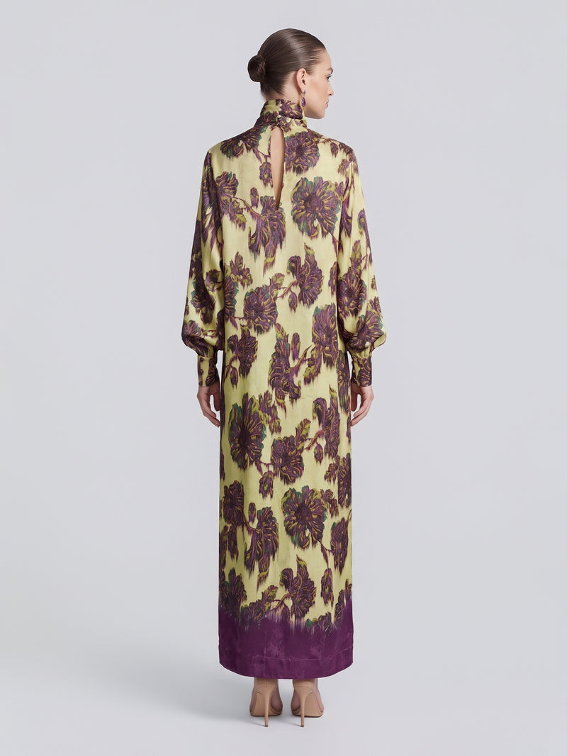 A woman with her hair in a bun models the Social Queen Art Floral Jacquard Maxi Dress, a long-sleeved, floor-length piece featuring purple accents and crafted from luxurious viscose jacquard, shown from the back against a plain light background.