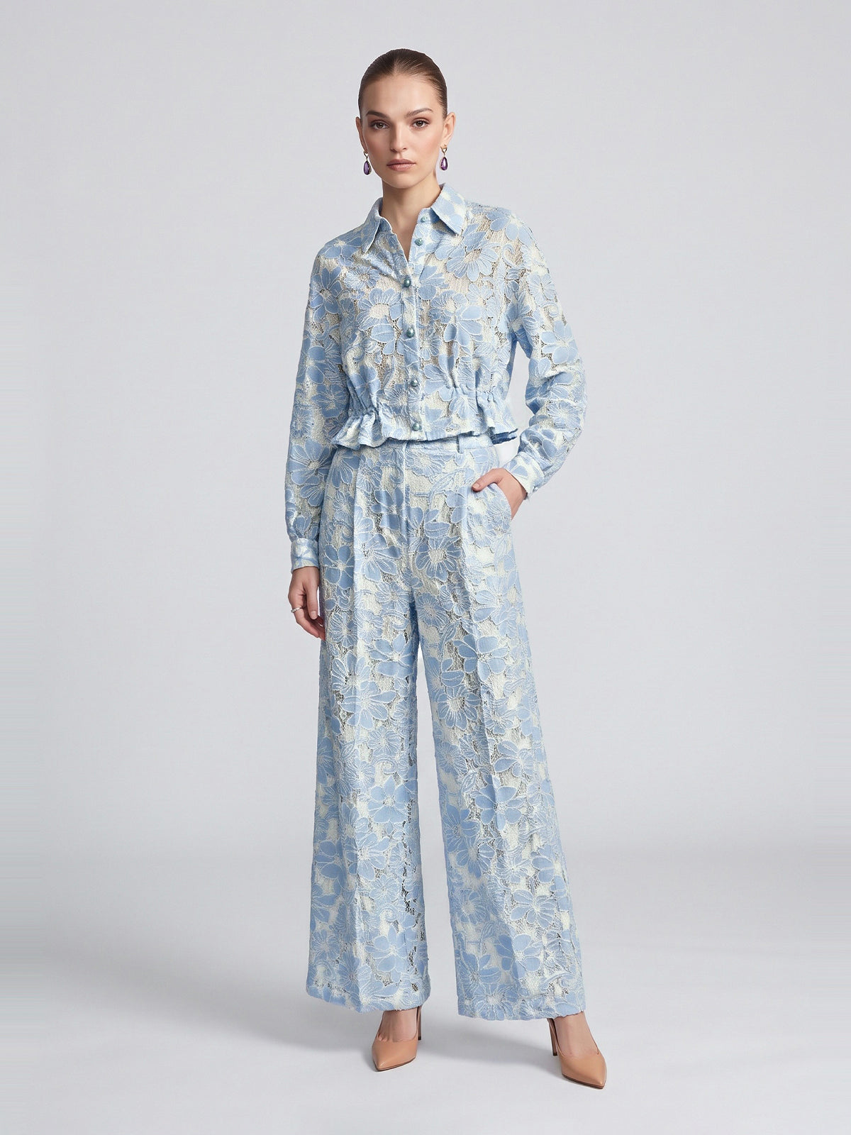 A model wears a light blue openwork floral lace long-sleeve button-up shirt with a ruffled hem paired with matching Floral Lace Wide-Leg Pants.