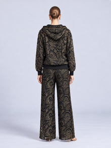 Back view of a person wearing the Paisley Embroidered Lace Hooded Jacket paired with matching wide-leg trousers, both in black cutout lace with gold-tone paisley embroidery.