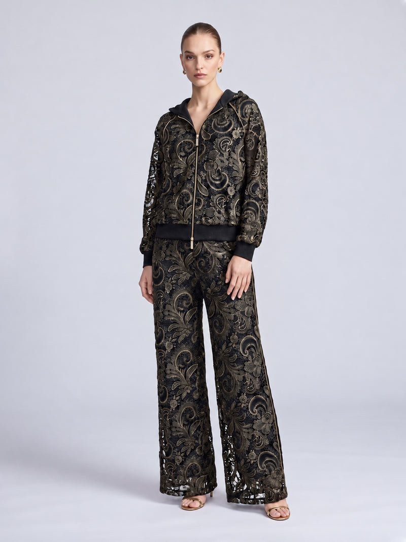 A model wears a black hooded jacket and matching Paisley Embroidered Lace Wide-Leg Pants, both featuring gold paisley embroidery and cutout lace panels.