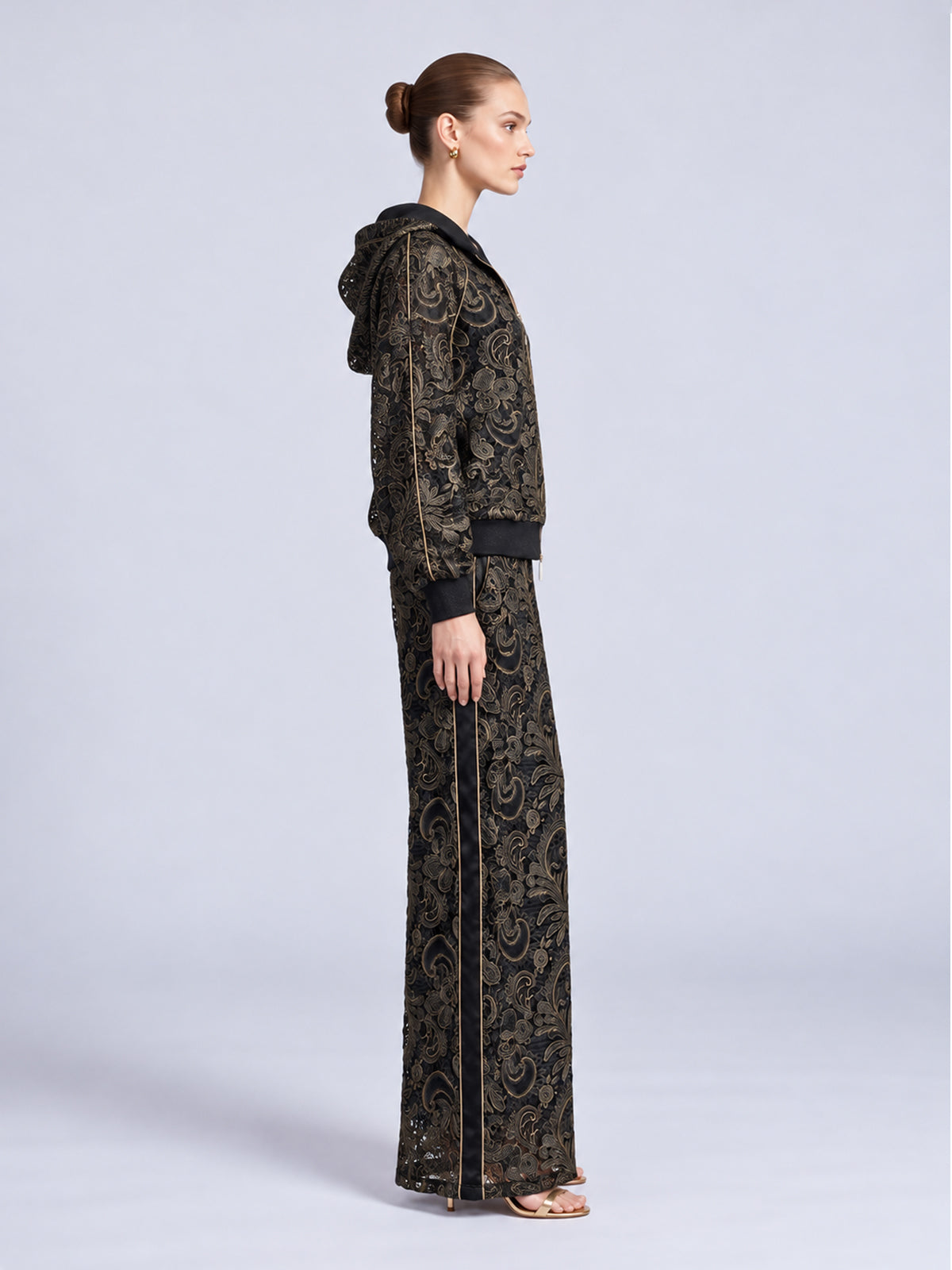 A side view of a person wearing a Social Queen Paisley Embroidered Lace Hooded Jacket in black and gold with matching wide-leg trousers featuring a black side stripe.