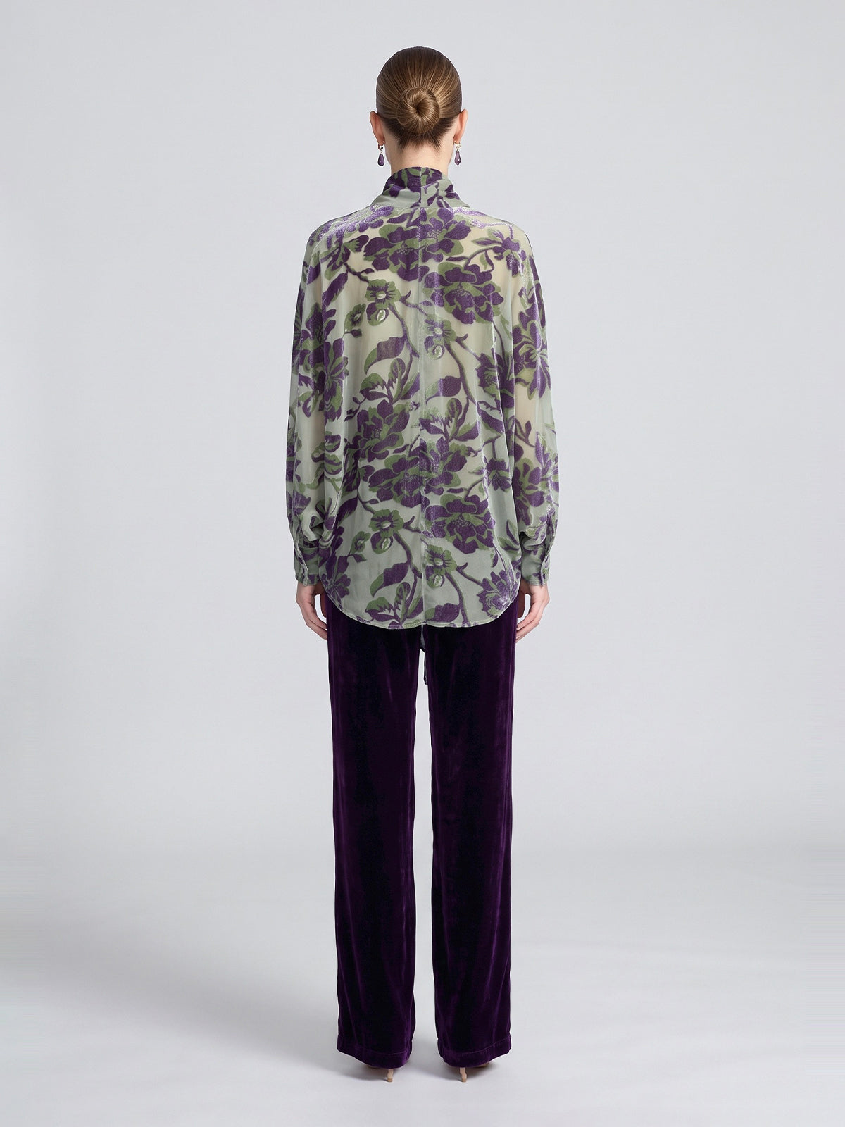 A person seen from behind wears a green, sheer long-sleeved shirt with a purple floral print and purple Velvet Wide-Leg Pants.