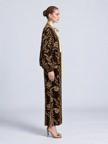 A woman wears a Social Queen Sequin Embroidered Velvet Midi Skirt and matching top with gold-tone sequin embroidery, styled with a beige neck-tie blouse and strappy heels.