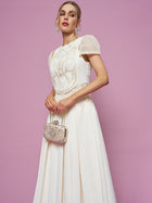 Woman wearing the Social Queen Appliqué Pearl Waffle Mesh Dress, holding a small ornate clutch, stands against a plain pink background.