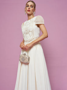 Woman wearing the Social Queen Appliqué Pearl Waffle Mesh Dress, holding a small ornate clutch, stands against a plain pink background.