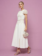 A woman wears the Social Queen Appliqué Pearl Waffle Mesh Dress with silver high-heeled sandals and an ornate small handbag, standing against a plain pink background.