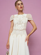 A woman stands against a pink background wearing the Social Queen Appliqué Pearl Waffle Mesh Dress, featuring floral embroidery, sheer details, an A-line silhouette, and holding a small purse in her right hand.