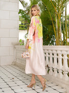 A woman wears the Social Queen Aquarelle Blooms 100% Mulberry Silk Dress and gold heels while standing on a tiled balcony with greenery, holding a small decorative handbag.