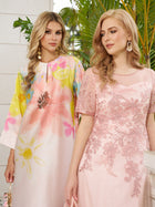Two women with long blonde hair stand together. One wears the Social Queen Aquarelle Blooms 100% Mulberry Silk Dress, featuring a watercolor floral print; the other wears a fitted pink floral embroidered wedding guest dress. Green plants are behind them.