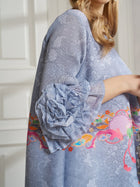 A person wears the Social Queen Art-Print Floral-Appliqué Pleated Dress, a comfortable light blue party dress featuring a large floral appliqué on the sleeve and vibrant embroidery near the hem.