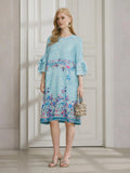 A woman stands indoors wearing the Social Queen Art-Print Floral-Appliqué Pleated Dress with ruffled sleeves, silver sandals, and a small handbag.