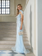 A woman wearing the Social Queen Artisanal Beaded Fringe High-Neck Gown stands on a staircase inside a building with large windows, holding a decorative clutch.