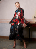 A woman poses indoors in the Social Queen Artistic Floral Print Ruffle Dress, featuring a long, flowing silhouette and vibrant floral patterns, standing beside a table with a single candleholder.