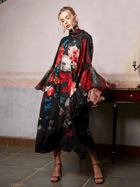 A woman poses indoors in the Social Queen Artistic Floral Print Ruffle Dress, featuring a long, flowing silhouette and vibrant floral patterns, standing beside a table with a single candleholder.