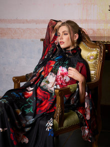 A woman in the Social Queen Artistic Floral Print Ruffle Dress sits on an ornate chair, her arm draped over the back, gazing to the side in a vintage-inspired room.