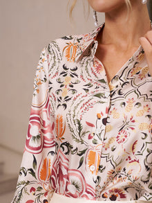 Close-up of a woman in the Social Queen Artistic Floral Print Silk Blouse, featuring a shiny, long-sleeved design with pink, orange, black, and green botanical patterns. The silk's pearlescent sheen catches the light; her face is partially out of frame.