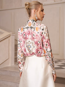 A woman with blonde hair in an updo wears the Social Queen Artistic Floral Print Silk Blouse and a white skirt, standing on stairs with her back mostly to the camera.