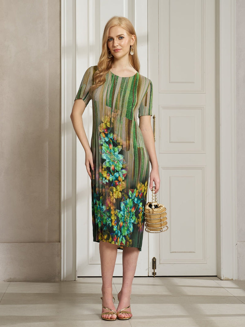 A woman stands indoors in the Social Queen Artistic Smudge Print Plissé Dress, a knee-length, short-sleeve pleated piece with vibrant ombre stripes and florals, paired with a gold bag and sandals.
