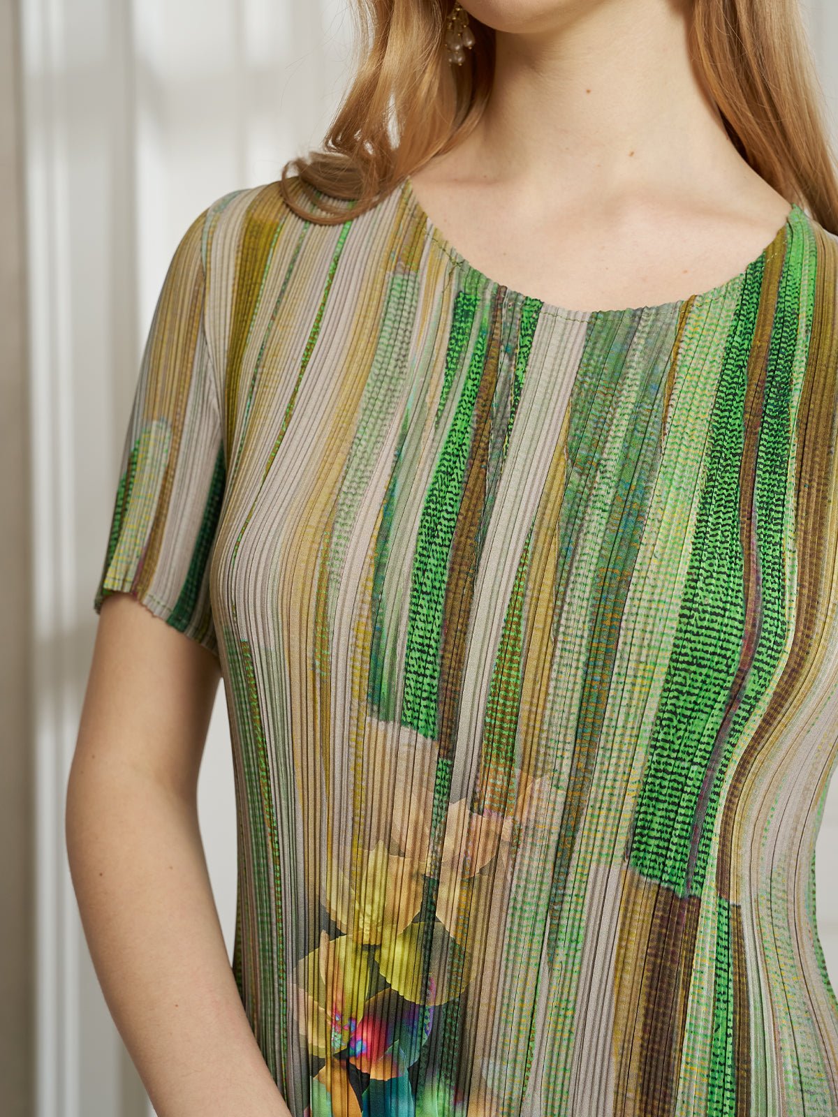 A woman wears the Artistic Smudge Print Plissé Dress by Social Queen—a short-sleeved silk style with vertical green, yellow, and beige stripes, plus a floral accent at the waist—ideal for effortless resort wear.