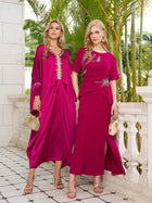 Two women pose side by side in Social Queen’s Asymmetric Beaded Mermaid Slit Dresses, holding handbags on a tiled terrace with lush greenery behind them.