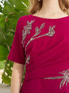 A woman wearing the Social Queen Asymmetric Beaded Mermaid Slit Dress stands before lush green foliage.
