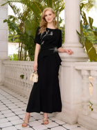 A woman in the Social Queen Asymmetric Beaded Mermaid Slit Dress stands on a tiled balcony, holding a small beige handbag, surrounded by lush plants and elegant columns.