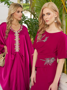 Two women in Social Queen's Asymmetric Beaded Mermaid Slit Dress stand before green plants, each accessorized with gold earrings.