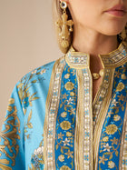 A woman wears the Social Queen Baroque Engineered-Print Cotton Dress, featuring blue and gold floral patterns with a mandarin collar, paired with large gold earrings; only her lower face and upper torso are shown.