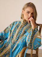 A woman in the Social Queen Baroque Engineered-Print Cotton Dress sits on a wooden chair, resting her chin on her hand and looking at the camera.