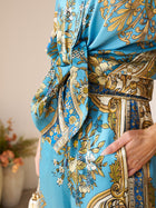Close-up of a person wearing the Social Queen Baroque Engineered-Print Silk Shirt, featuring intricate blue and gold designs, with one hand in their pocket and a blurred vase of flowers in the background.