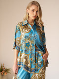 Woman wearing the Social Queen Baroque Engineered-Print Silk Shirt in blue and gold, styled with matching pants, standing indoors with one hand in her pocket.