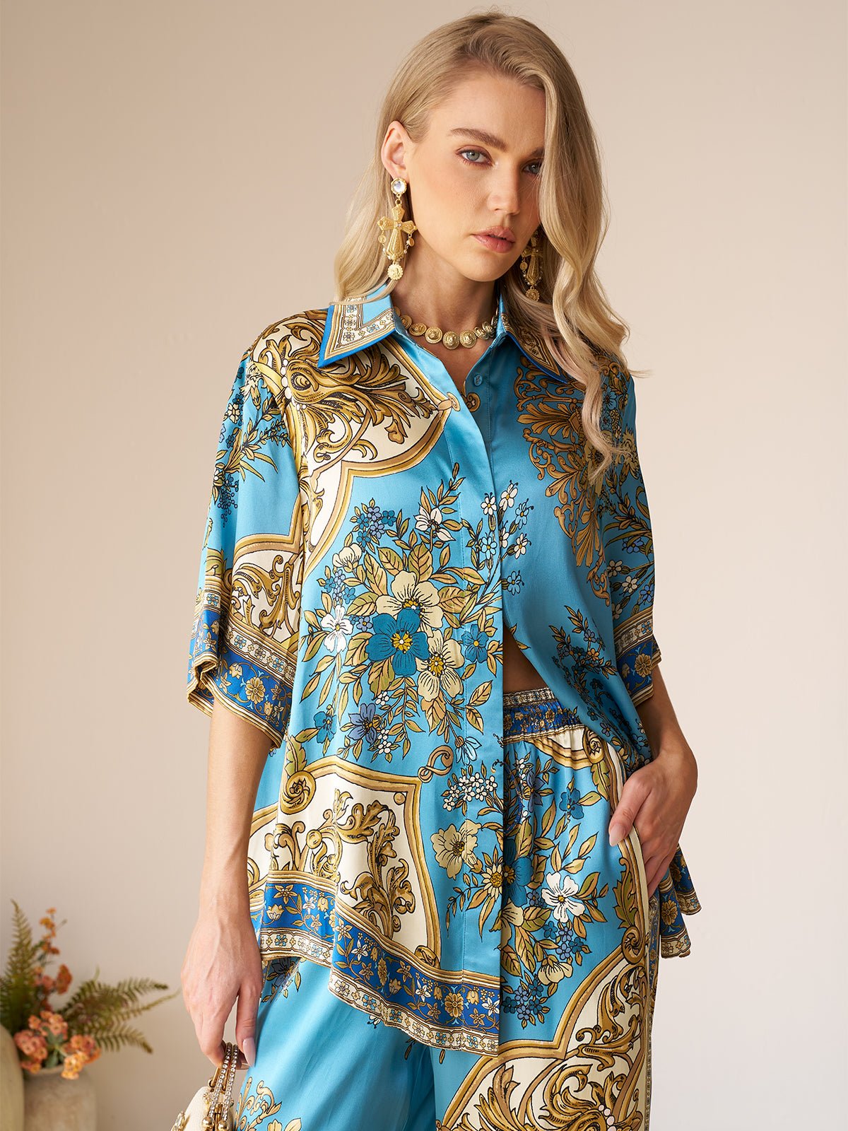 Woman wearing the Social Queen Baroque Engineered-Print Silk Shirt in blue and gold, styled with matching pants, standing indoors with one hand in her pocket.