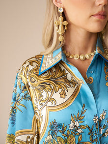 Woman shown from the shoulder up wearing the Social Queen Baroque Engineered-Print Silk Shirt, accessorized with a gold medallion necklace and ornate gold cross-shaped earrings.