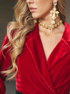 A woman with long wavy blonde hair wears a red velvet blazer, the Social Queen Baroque Medallion Necklace, and a large gold cross earring.