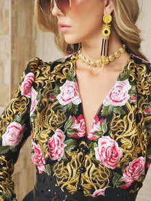 A woman wearing sunglasses, gold earrings, a Social Queen Baroque Medallion Necklace, and a black top with pink rose and gold embroidery.