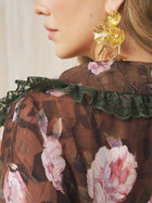 Close-up of a woman wearing Social Queen's Baroque Petal Pearl Drop Earrings and a sheer brown floral blouse with green lace-trimmed collar.
