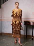 A woman stands indoors in the Social Queen Baroque Velvet Fringe Set—gold and brown silk burnout velvet with baroque patterns and fringe—paired with a handbag and gold heels for an elegant wedding guest look.