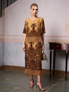 A woman stands indoors in the Social Queen Baroque Velvet Fringe Set—gold and brown silk burnout velvet with baroque patterns and fringe—paired with a handbag and gold heels for an elegant wedding guest look.