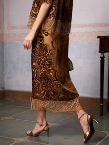A woman in the Baroque Velvet Fringe Set by Social Queen and gold high-heeled sandals walks on a tiled floor near a small table.