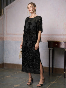 A woman wearing the Social Queen Baroque Velvet Fringe Set stands indoors by a wooden table with a small clutch—an elegant choice for a wedding guest.