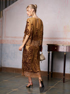 A woman stands indoors in the Social Queen Baroque Velvet Fringe Set, gold heels, and a small bag, facing away from the camera—the perfect wedding guest outfit.