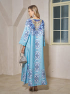 A woman in the Social Queen Beaded Baroque A-Line Dress, featuring a striking blue baroque print—ideal for resort wear.