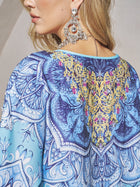 A woman wears the Social Queen Beaded Baroque A-Line Dress featuring blue patterns with intricate yellow and pink embroidery on the back, styled with large silver earrings—perfect as a chic wedding guest outfit.