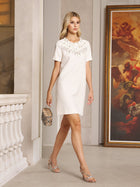 A woman in a Social Queen Beaded Collar A-Line Mini Dress holds a small purse as she walks indoors past a classical painting and decorative railing.