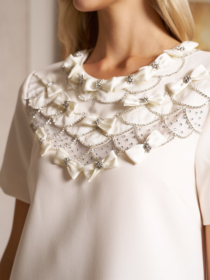 Close-up of a woman wearing the Social Queen Beaded Collar A-Line Mini Dress, featuring rows of satin bows and sparkling rhinestone chains near the neckline.